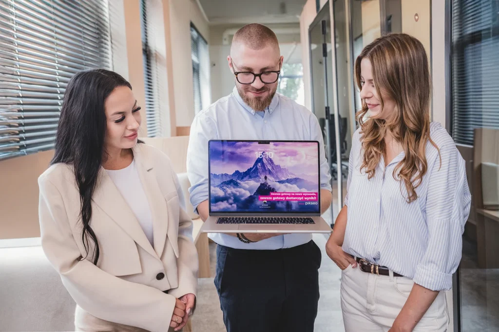 Trzy osoby oglądają stronę internetową na laptopie w biurze PIKSEO